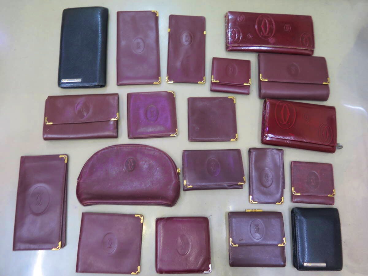 A flat lay of many Cartier wallets and small leather goods, mostly burgundy with two black pieces, arranged on a light surface.