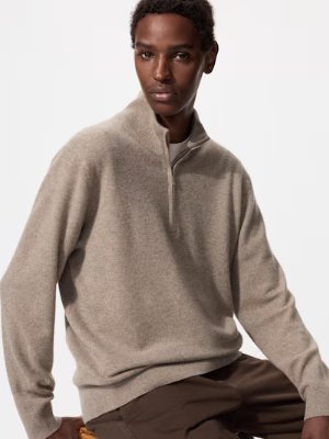 Model wearing a beige cashmere half-zip sweater seated against a plain white background.