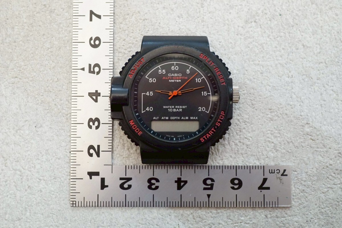 Top-down photo of the CASIO watch face (analog hands and small digital window) placed next to two measuring rulers.