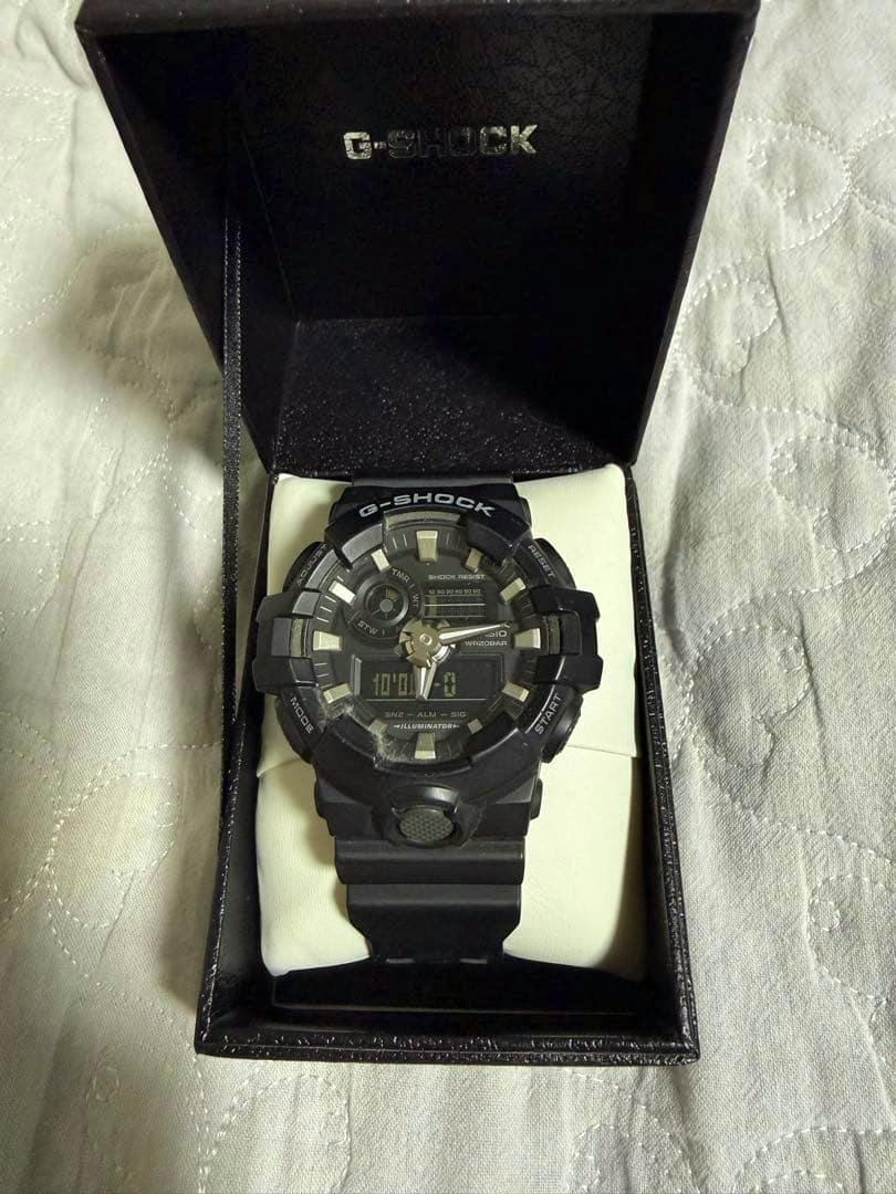 Black CASIO G-SHOCK analog-digital wristwatch displayed in its open box on a quilted surface.