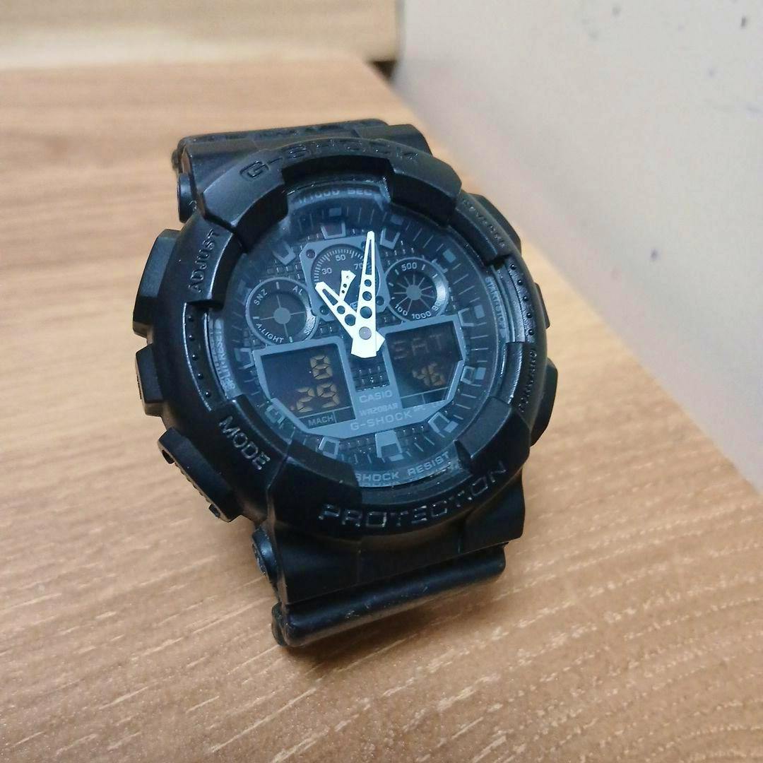 Black Casio G-SHOCK GA-100 analog-digital men's wristwatch on a wooden surface showing the watch face and strap.