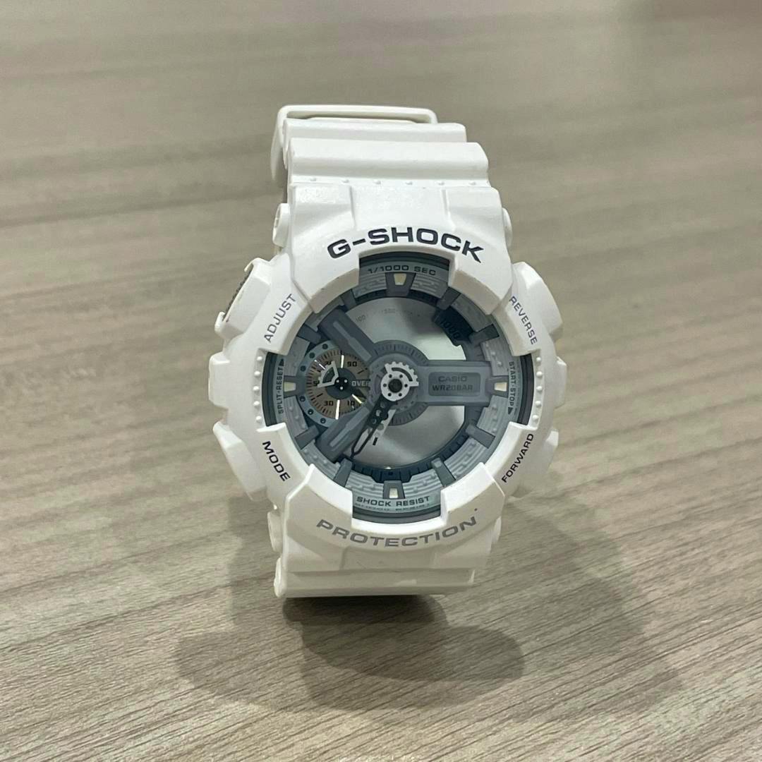 A white Casio G-SHOCK GA-110C wristwatch placed upright on a wood surface showing the face and strap.