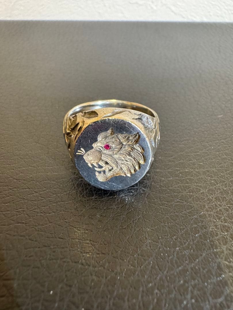 Front view of the sterling silver ring showing a round face engraved with an animal head and a red stone eye.