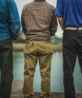Three men shown from the back wearing men's Cat Worker Pants in tan, dark green, and black.