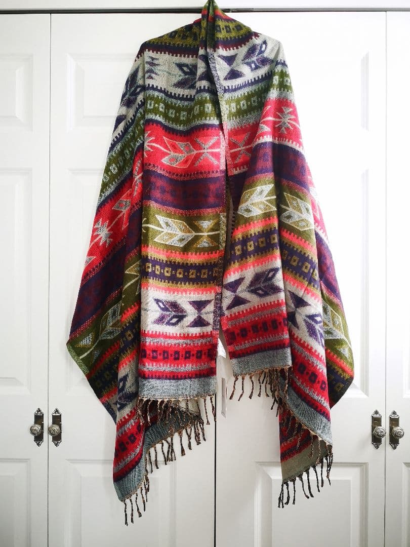 A polyester blanket/throw with colorful ethnic geometric patterns and fringed edges hanging against white closet doors.