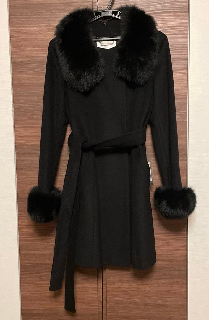 Black women's wool coat with a fox-fur collar and fur cuffs hanging on a hanger.