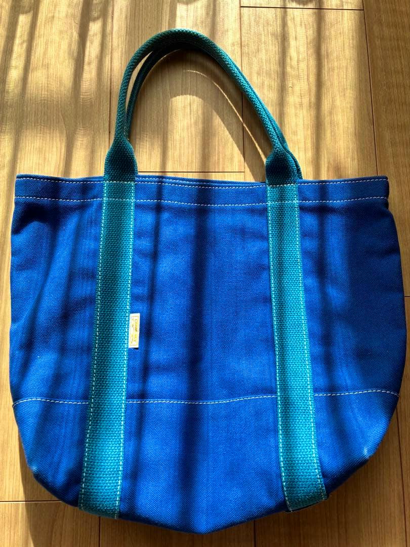 Blue canvas CEDAR KEY tote bag with teal handles laid flat on a wooden floor.