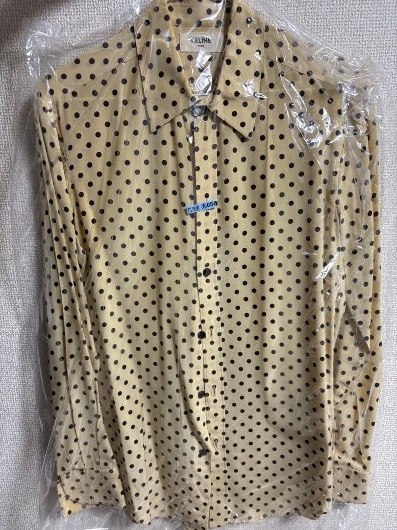 Beige polka dot men's silk shirt (CELINE) shown in a clear plastic cover against a textured wall.