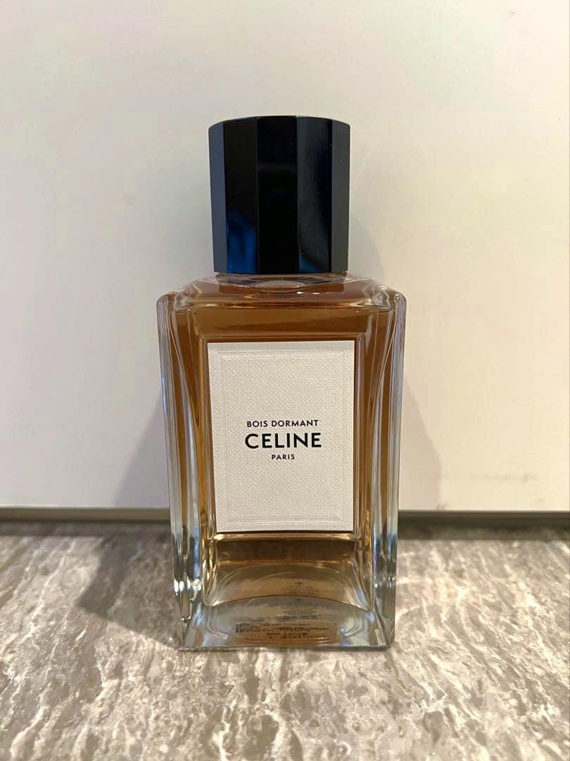 Front view of a rectangular CELINE Bois Dormant perfume bottle with amber liquid and a black faceted cap, label visible.