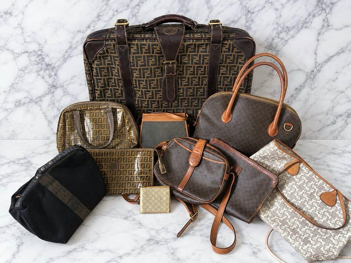 A set of assorted bags including a large FENDI-patterned travel bag and several smaller handbags and pouches displayed on a marble surface.