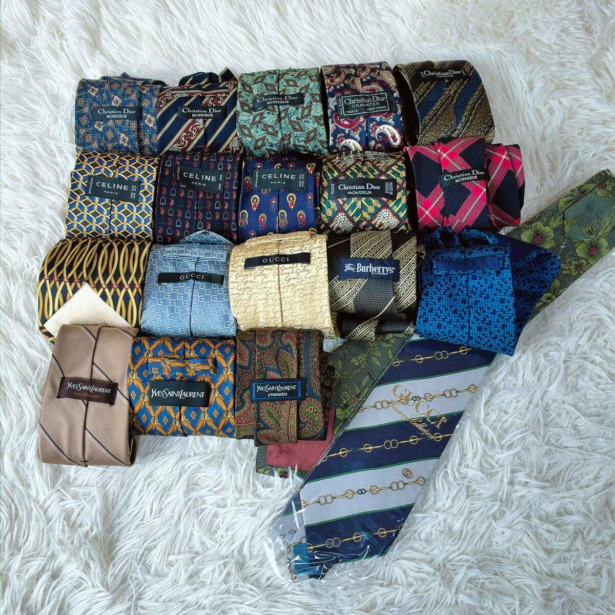 Multiple rolled silk neckties of various patterns and brands arranged on a white faux-fur background.