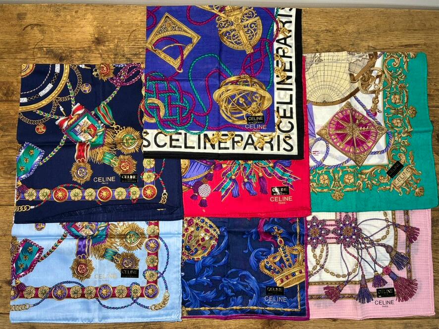 Seven folded CELINE patterned silk scarves/handkerchiefs arranged on a wooden surface showing various colorful prints.