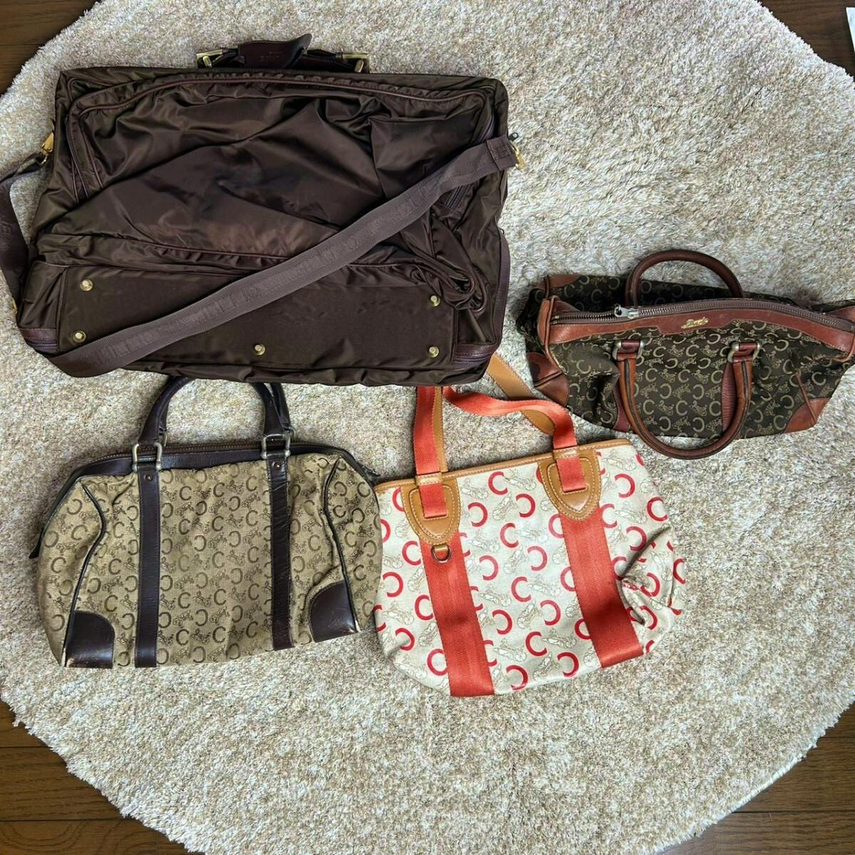 Four CELINE bags from the Macadam set—a large brown travel bag, two small C-pattern Boston bags, and a cream-and-red tote—laid out on a round beige rug.