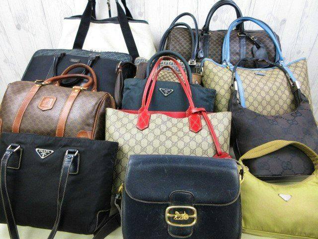 A grouped display of multiple branded handbags and totes in various materials (canvas, leather, nylon) arranged together.