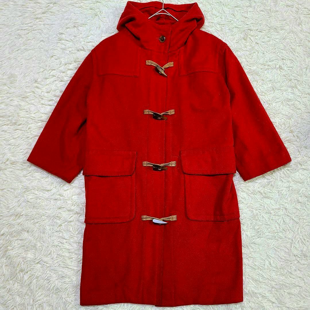 Red long duffle coat with a hood and toggle closures laid flat on a light textured surface.