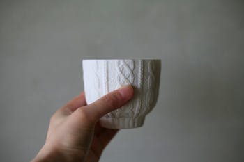 A hand holding a white textured Trace Face vessel against a plain neutral background.