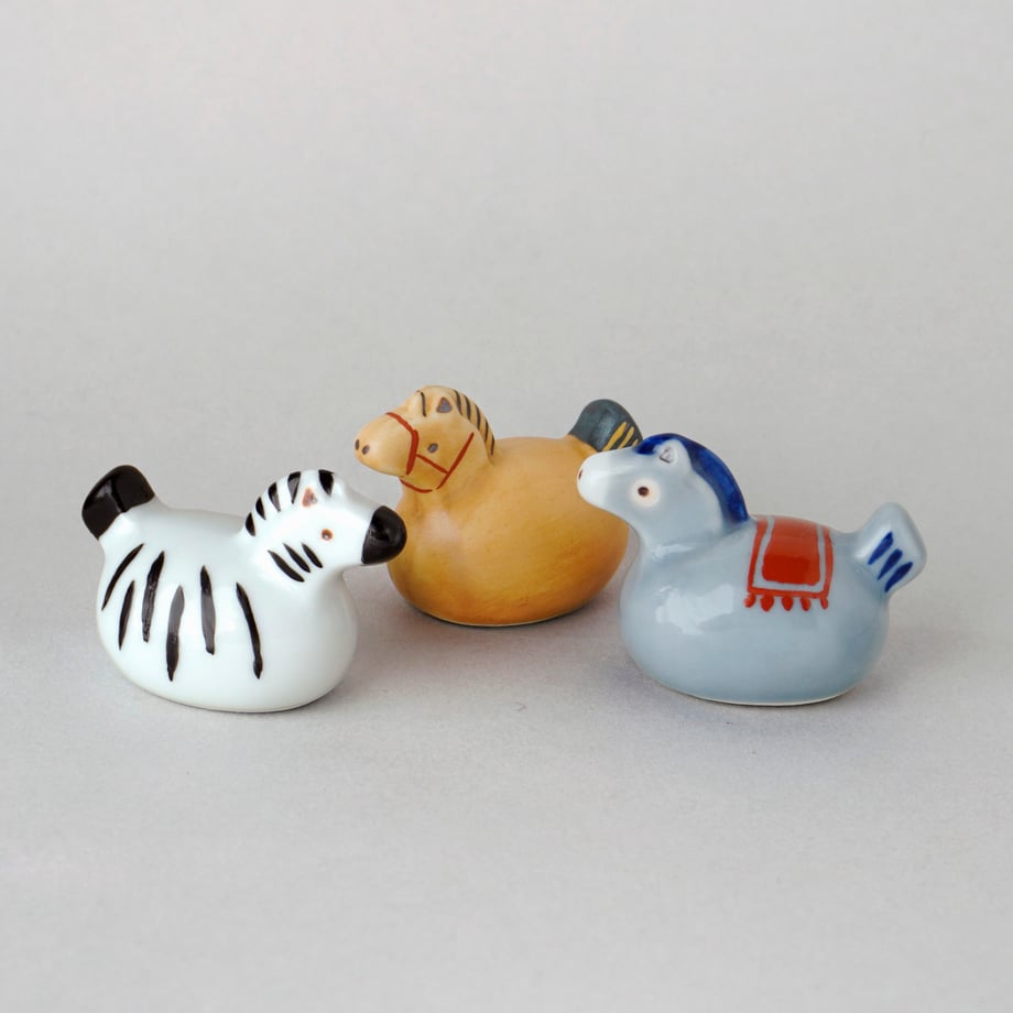 Three ceramic horse-shaped chopstick rests in white, tan, and blue on a plain background.