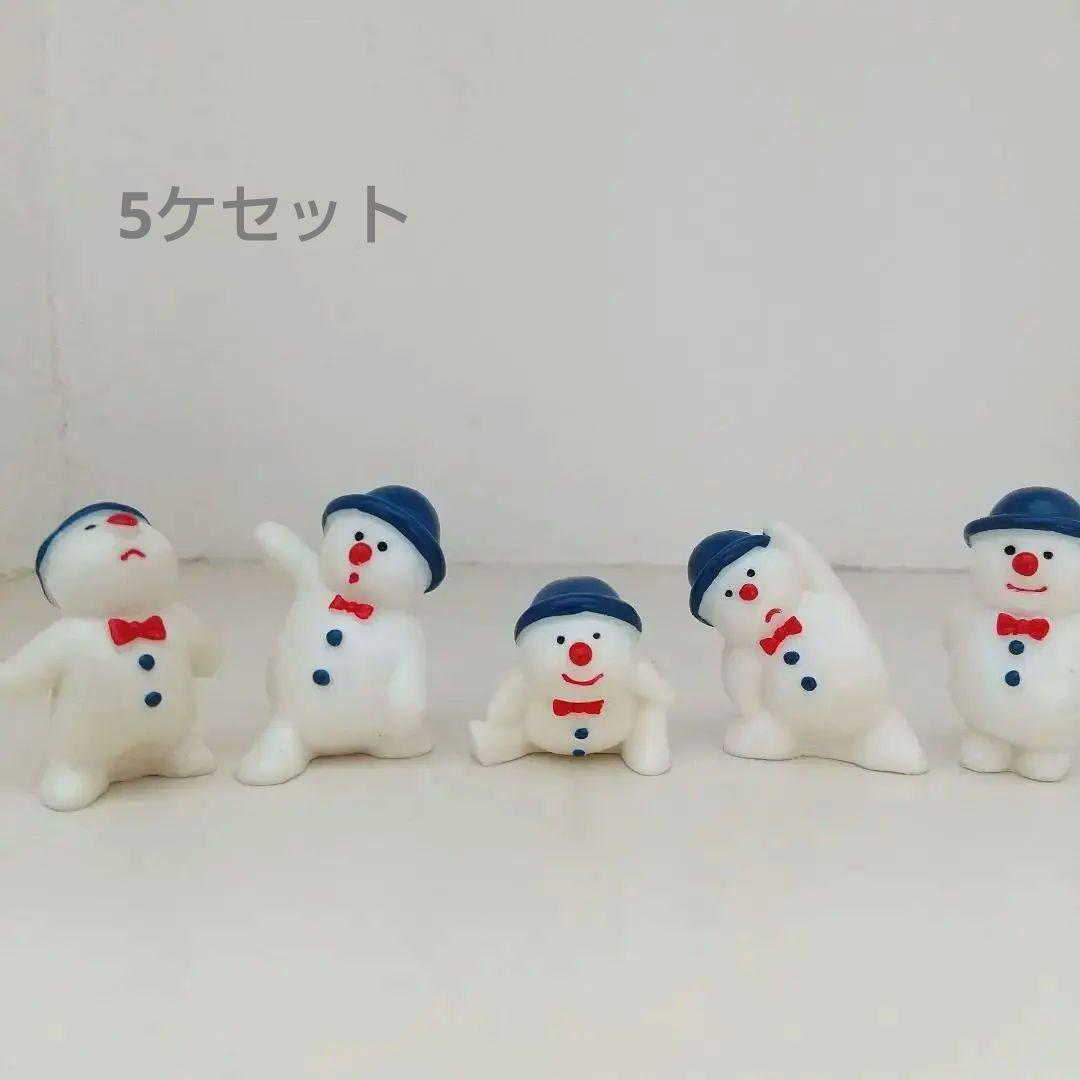 Five small white snowman ceramic figurines wearing blue hats and red bow ties lined up against a white background.