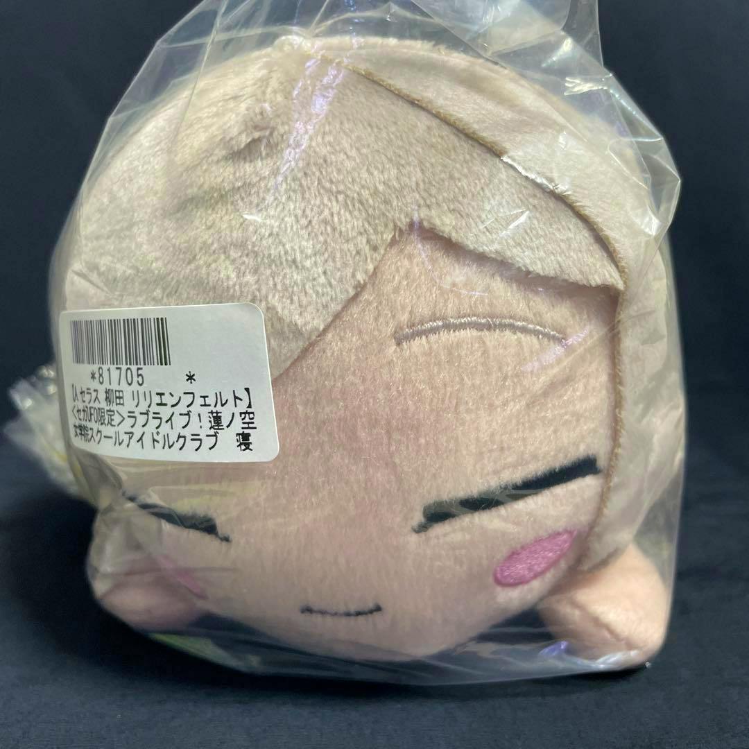 Front view of the セラス柳田リリエンフェルト 寝そべり ぬいぐるみ オンライン限定Ver. plush inside a clear plastic bag, showing its face and a barcode sticker.
