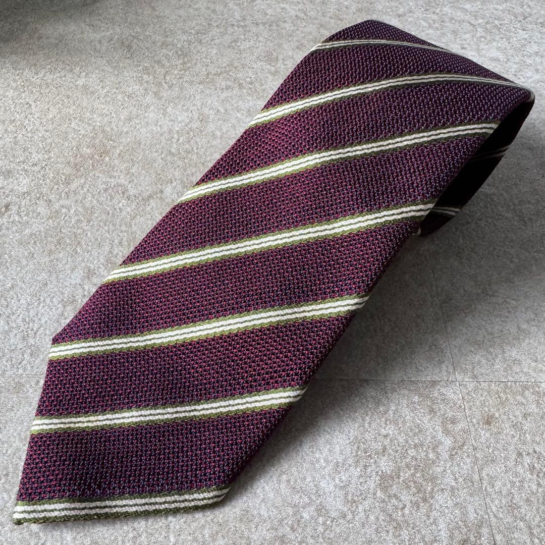 Maroon regimental-striped Cesare Attolini silk necktie laid flat on a light textured surface.