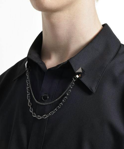 A metal chain lapel brooch with two pyramid studs and double chains attached to a shirt collar.