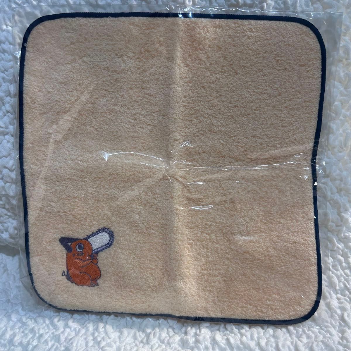 Unopened beige Chainsaw Man Imabari mini polyester handkerchief with a small Pochita illustration in the lower-left, shown in plastic packaging.