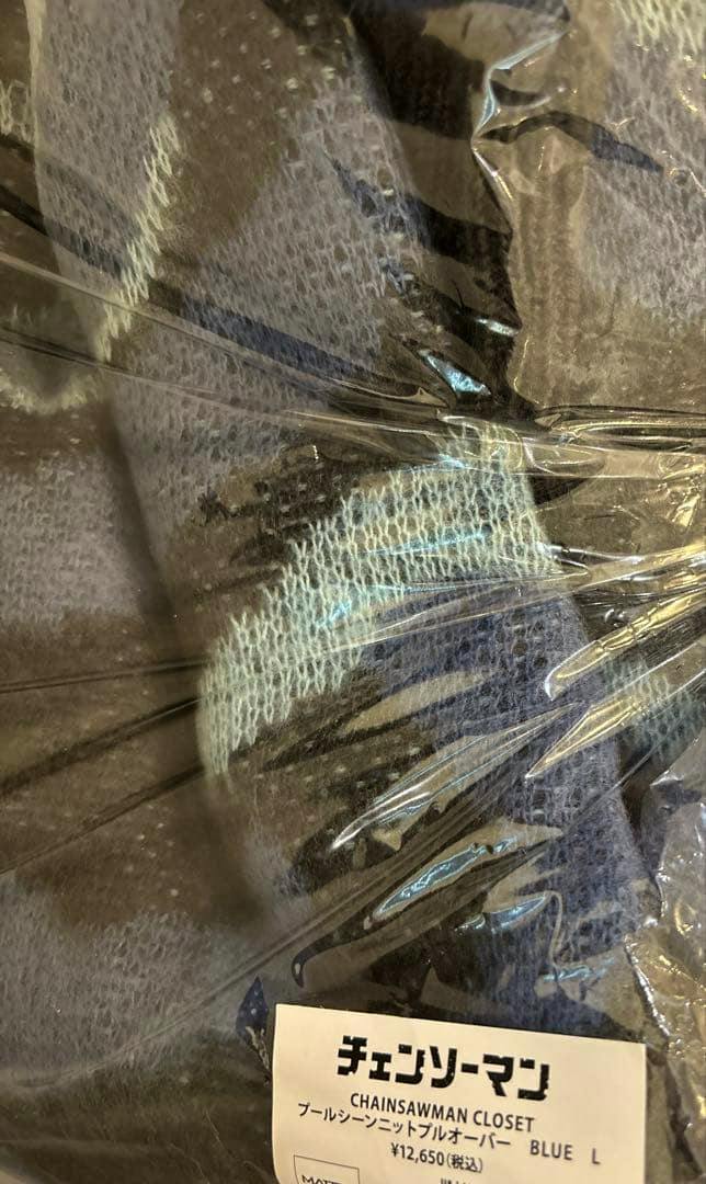 A folded ChainsawMan “Pool Scene” knit pullover in blue inside clear plastic packaging with its label showing size L.
