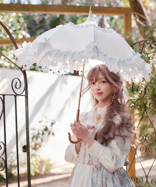 A model outdoors holding a white frilly Chalmiere×Apleberute umbrella with lace ruffles.