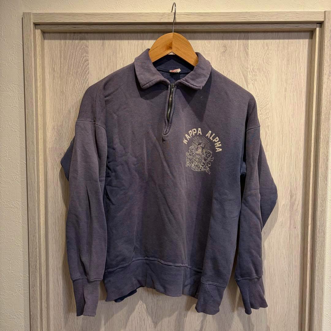 Front view of a vintage Champion half-zip eggplant-navy sweatshirt hanging on a wooden hanger against a light wood background, showing the chest print and collar.