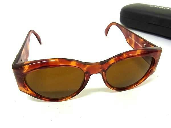 Brown tortoiseshell CHANEL plastic sunglasses with brown lenses shown with a case in the background.