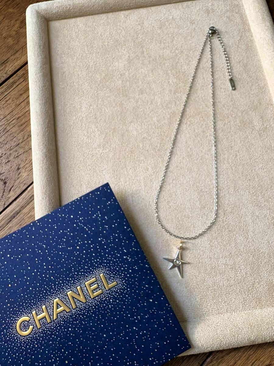 Silver chain necklace with a small silver star charm displayed on a beige tray next to a blue CHANEL box.