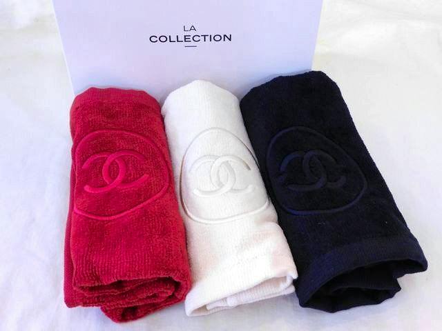 Three rolled CHANEL face towels in red, white, and navy placed in front of a box labeled "LA COLLECTION".