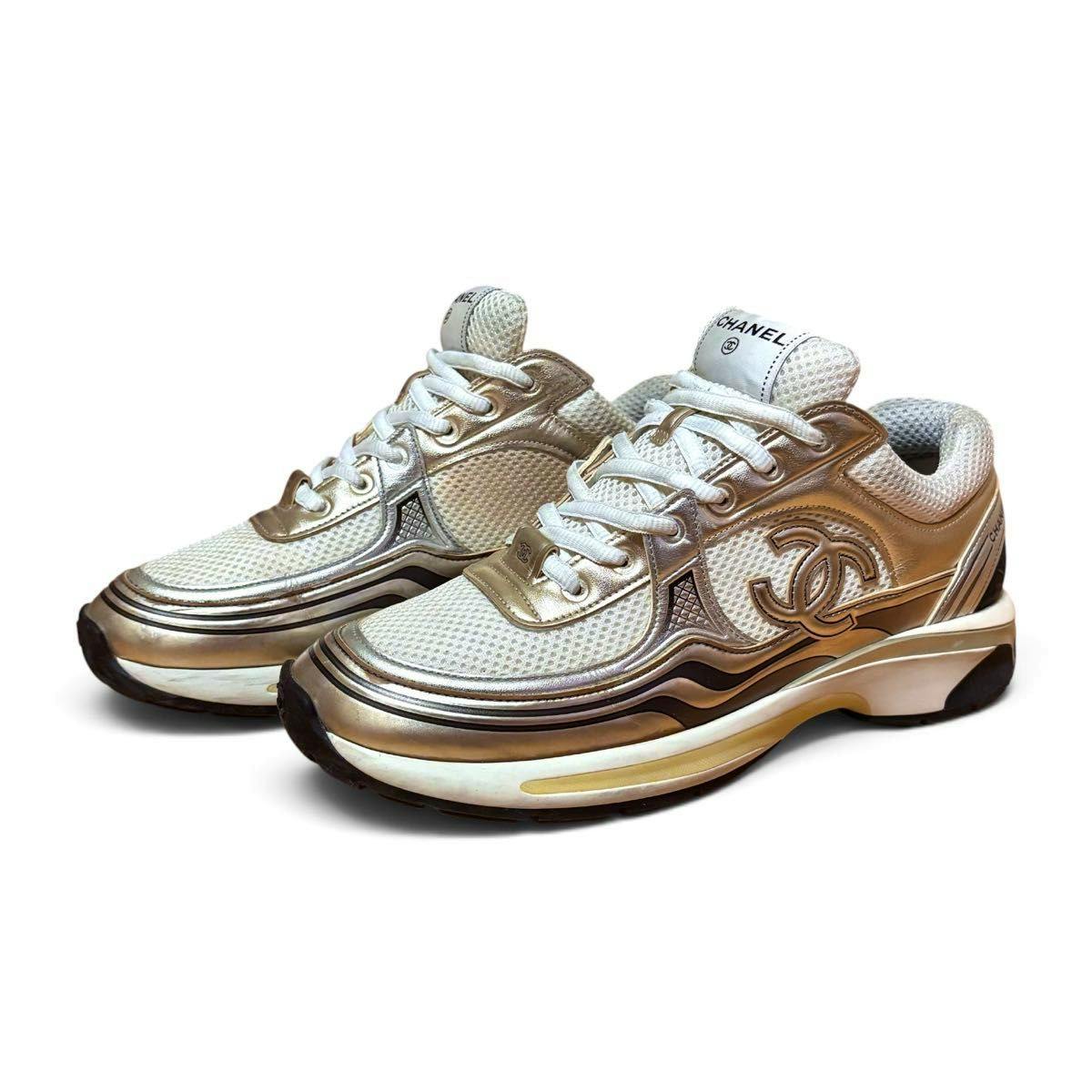 Pair of white and gold Chanel mesh sneakers with CC logo shown at a three-quarter angle.