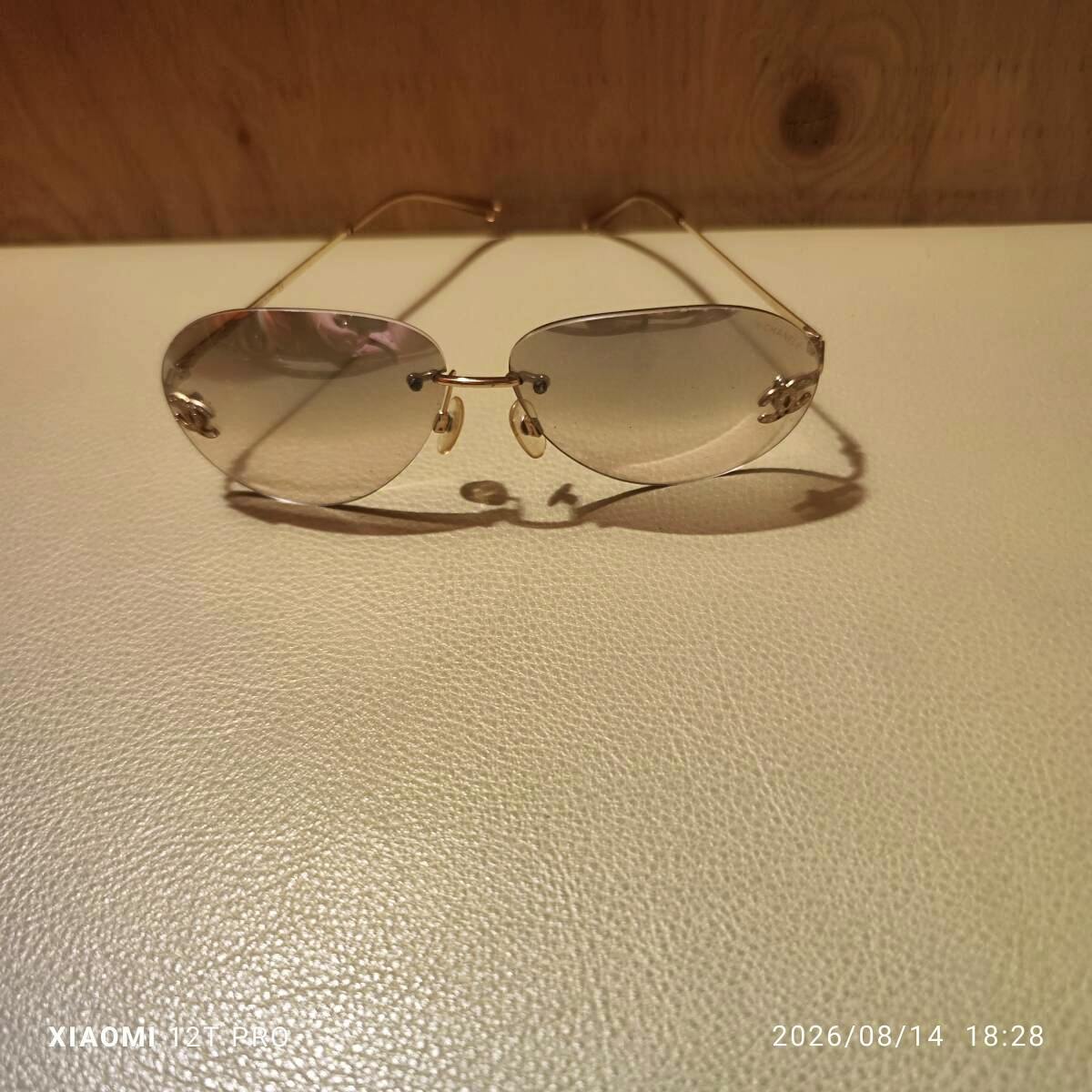 Rimless CHANEL sunglasses with gold temples and gradient lenses placed on a light surface.