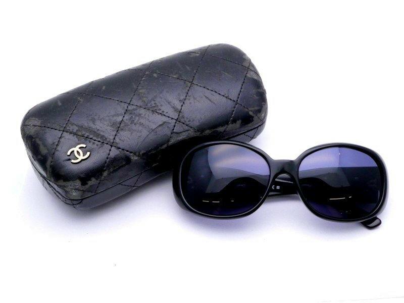 Black Chanel plastic full-rim sunglasses with dark lenses shown next to a quilted black Chanel case bearing a CC logo.