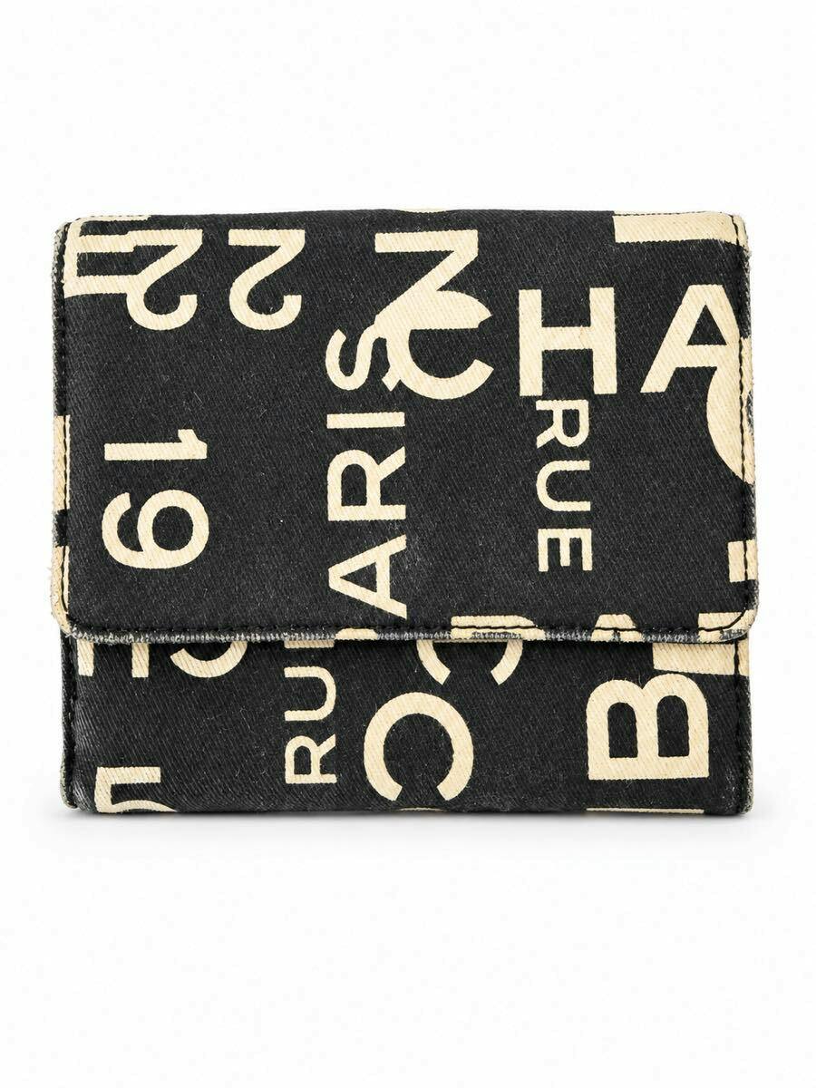 Front view of a black CHANEL canvas bi-fold wallet with cream logo pattern on a white background.