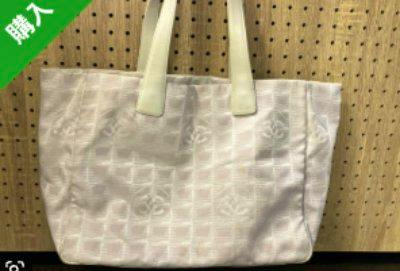 Light-colored CHANEL canvas tote bag with two shoulder handles photographed against a pegboard background.