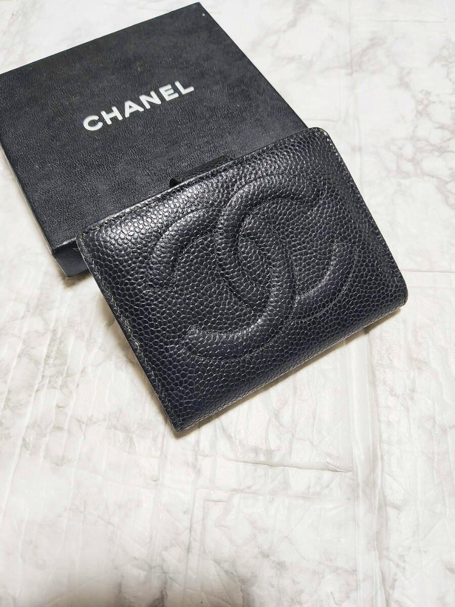 Black Chanel caviar leather wallet with a large embossed CC logo shown on a white surface next to a Chanel box.