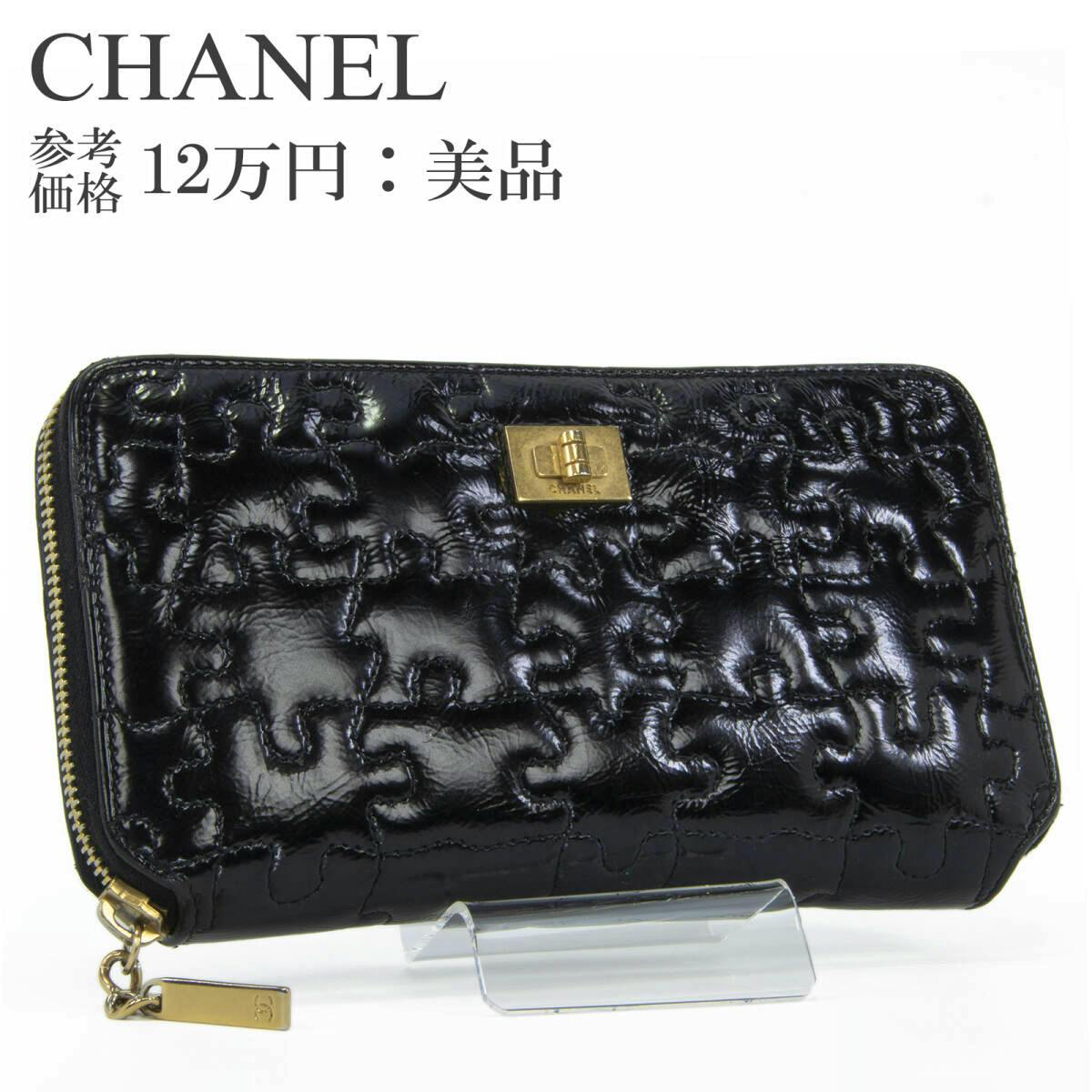 Black CHANEL long zip-around wallet in enamel leather with puzzle stitching and gold hardware displayed on a clear stand.