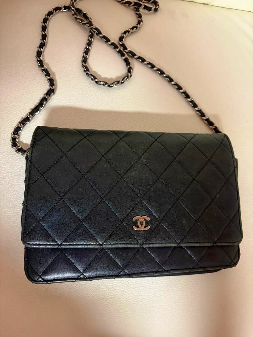 Black Chanel chain wallet bag in quilted cow leather with interwoven leather-and-chain strap and CC logo shown flat on a light surface.