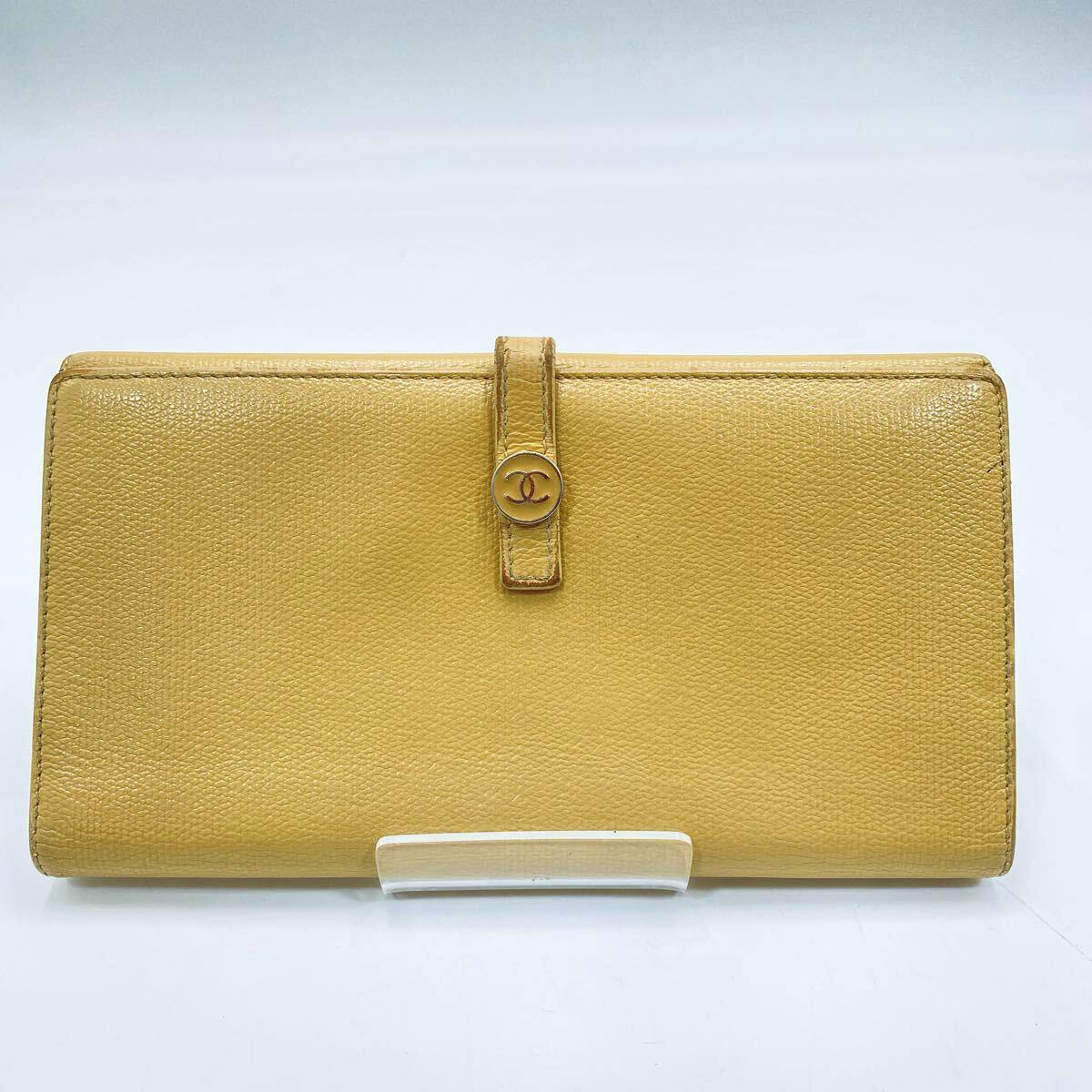 Front view of the beige CHANEL cow leather long bi-fold wallet with a strap and gold CC button displayed on a clear stand.