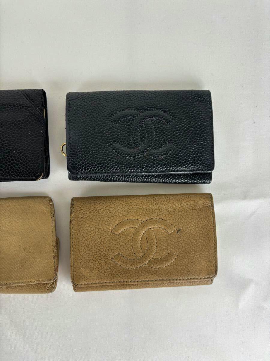 Beige Chanel key case in caviar leather with an embossed CC logo placed on a white background next to other key cases.