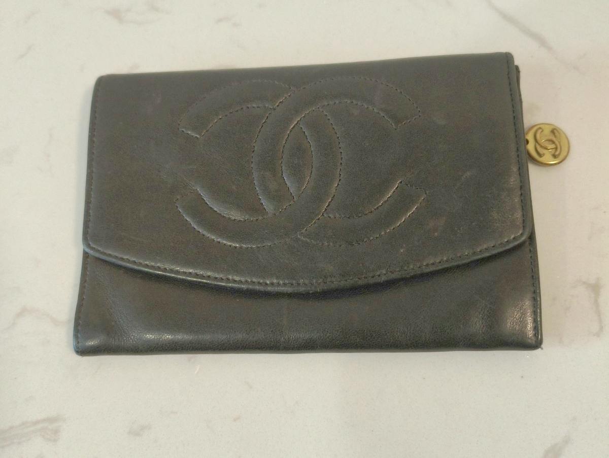 Black CHANEL two-fold (bi-fold) lambskin wallet showing the front with stitched interlocking CC logo and a round gold charm.