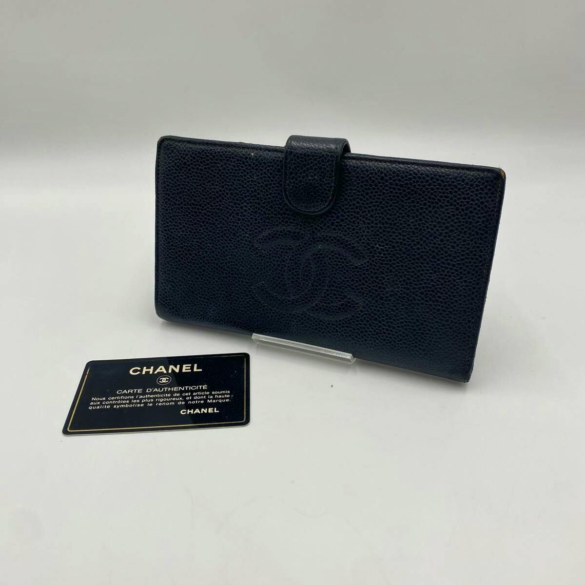 A dark pebbled leather CHANEL long wallet with embossed CC logo displayed upright next to a CHANEL authenticity card on a white background.