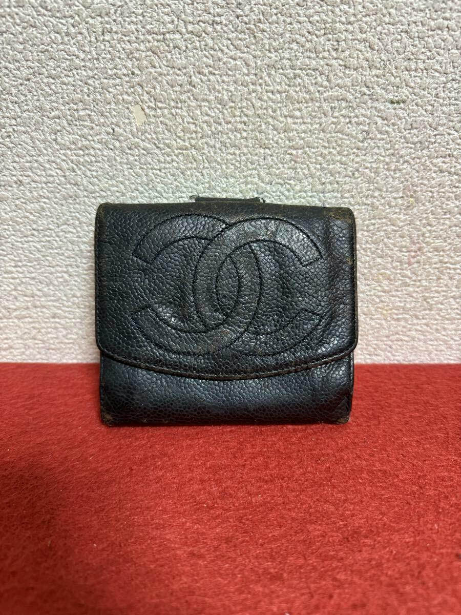 Front view of a black CHANEL caviar-skin wallet with a stitched double-C logo placed on a red surface.