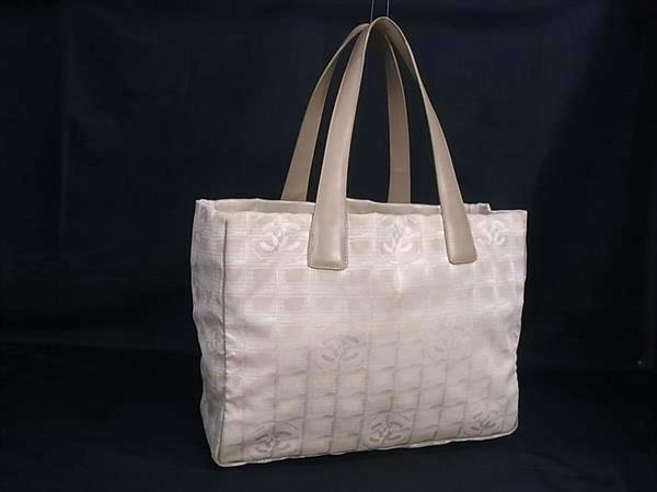 Beige Chanel nylon-canvas tote bag with leather handles and Coco logos, shown on a black background.