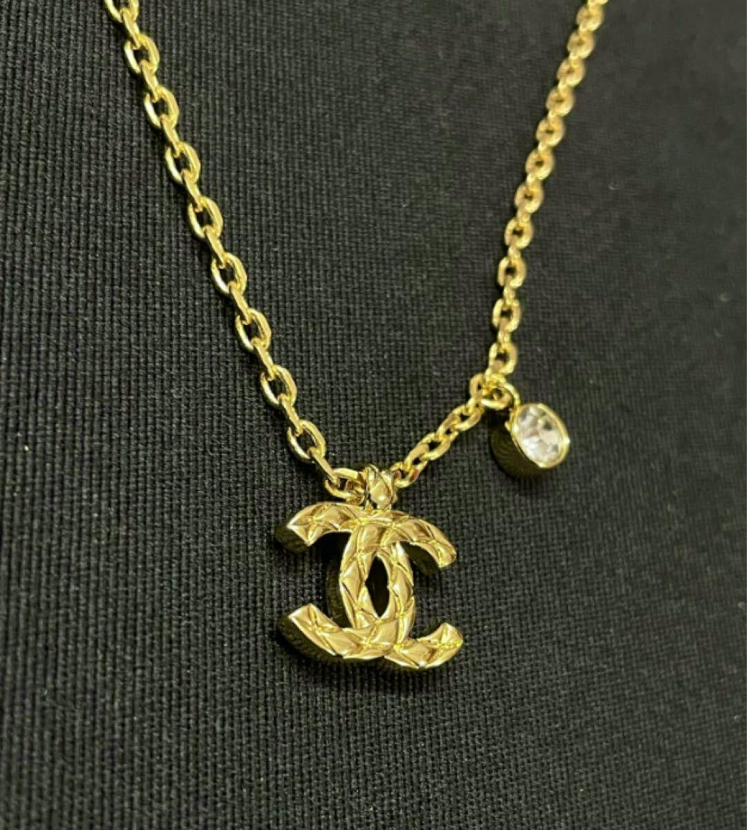 Close-up of a gold-color Chanel double-C motif pendant necklace with a small round crystal charm on a black background.