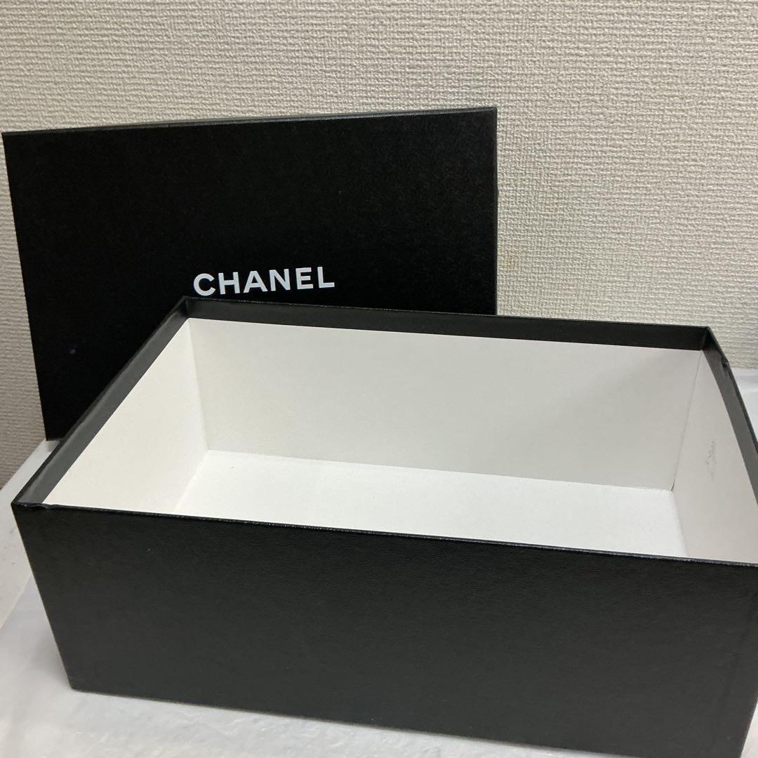 Open black CHANEL paper box with white interior and the lid behind showing the CHANEL logo.
