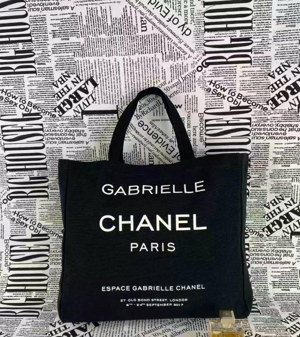 Front view of a black CHANEL Gabrielle canvas tote bag with white "GABRIELLE CHANEL PARIS" lettering.