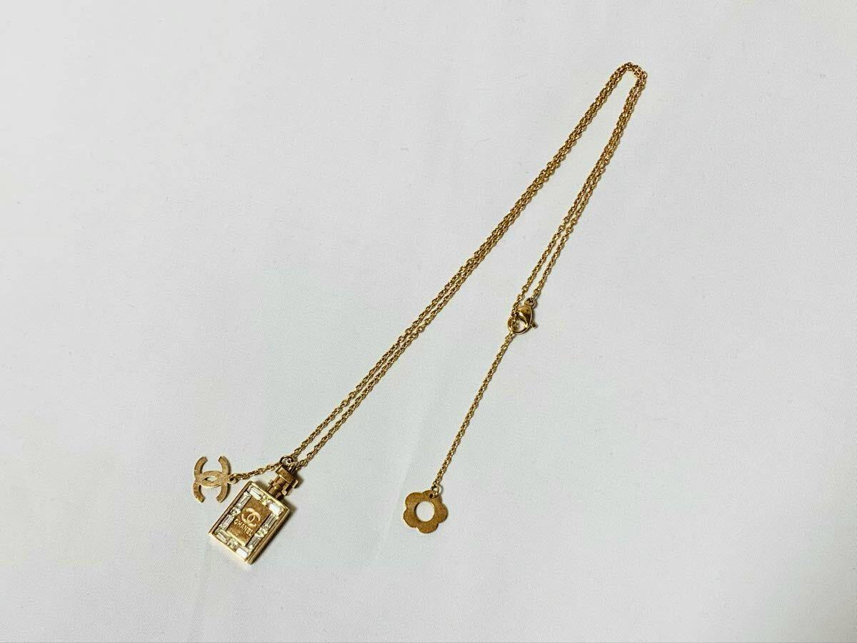 Gold CHANEL necklace laid on a white background showing a perfume-bottle charm, CC logo charm, and a small flower-shaped charm.